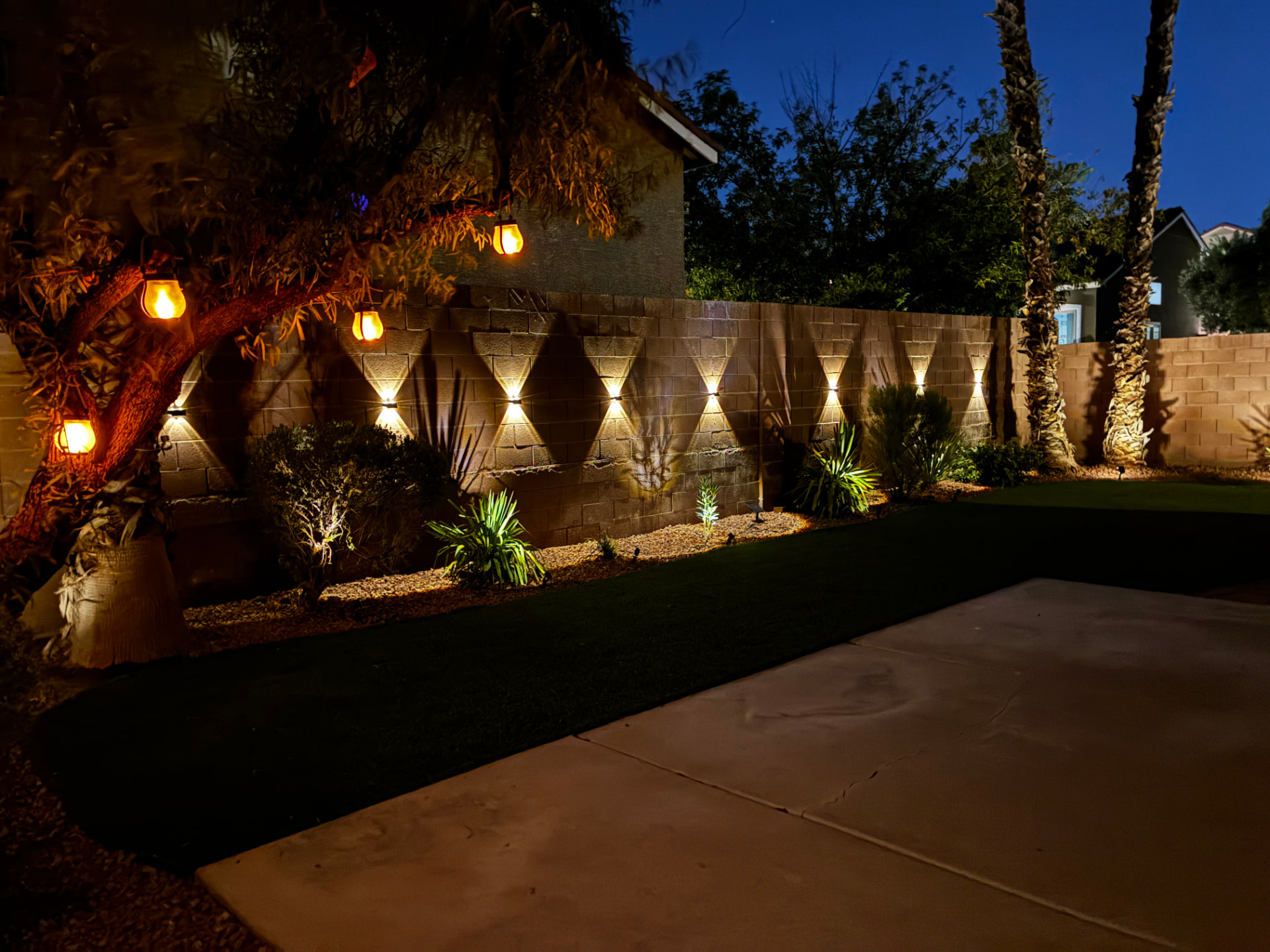 Backyard at dusk with wall uplighting and turf lawn